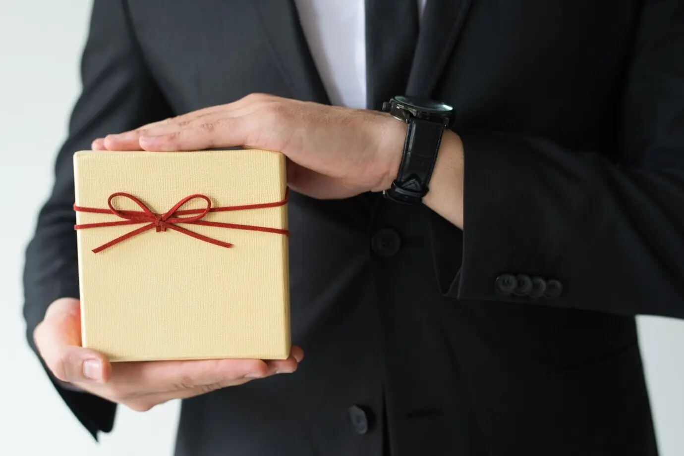 Close-up view of a man wearing a wristwatch holding a gift box.