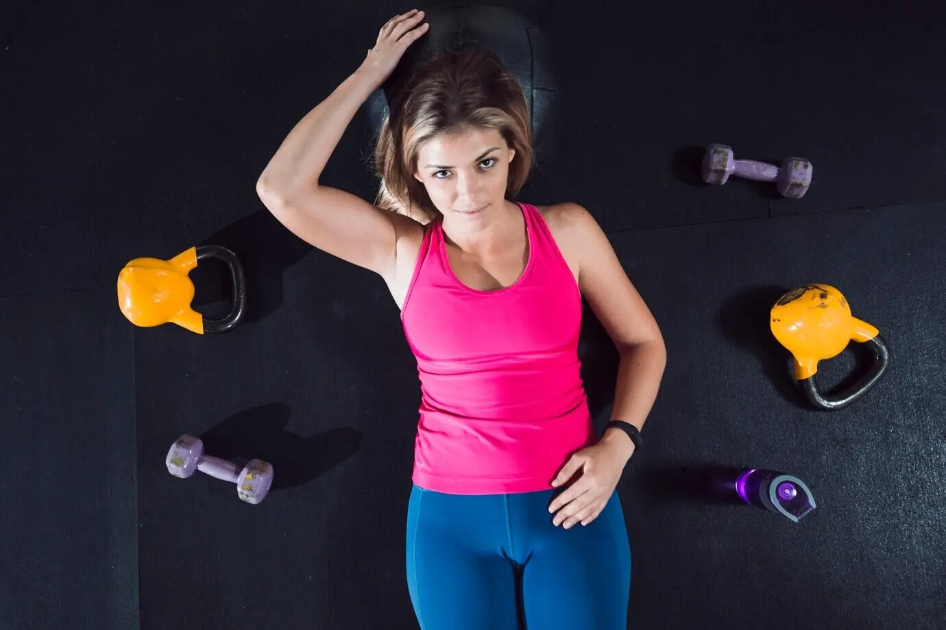 Overhead view of a fit woman relaxing on the floor near exercise equipment.